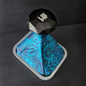 May include: A black gear shift knob with a geometric design and the letters "III" on top, sitting on a blue and black patterned gear shift boot.