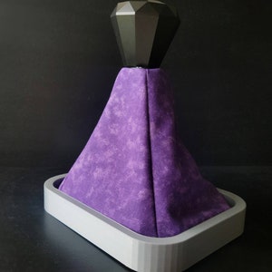 May include: Purple fabric gear shift boot with a black diamond-shaped knob. The boot is attached to a grey base.