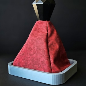 May include: A red suede gear shift boot with a black diamond-shaped knob. The boot is attached to a gray plastic base.