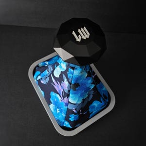 May include: A black diamond-shaped gear shift knob with the letters "LW" on top, sitting on a blue and black floral patterned gear shift boot.