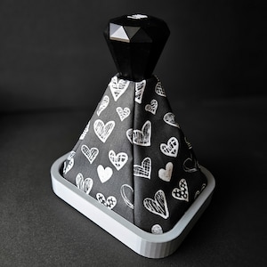 May include: A black and white patterned gear shift knob with a black diamond-shaped top. The knob is on a white base.