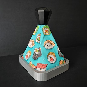 May include: A grey and black 3D printed gear shift knob with a black diamond-shaped top. The knob is covered in a blue fabric with a pattern of cartoon sushi rolls.