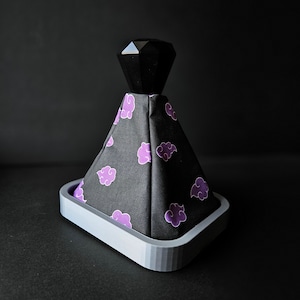 Peut inclure: Un pommeau de levier de vitesses noir et violet avec un dessus en forme de diamant et un motif nuage. Le pommeau est en tissu et a une base grise.