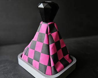 May include: A black and pink checkered gear shift knob with a black diamond-shaped top. The knob is mounted on a gray base.