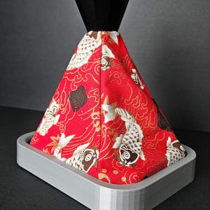 Peut inclure: Un pommeau de levier de vitesses recouvert d'un motif rouge, blanc et noir avec une base noire. Le motif représente des carpes koï et des vagues.