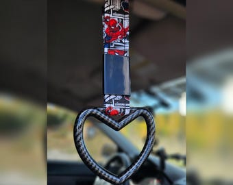 May include: A car grab handle with a heart-shaped grip. The strap features a Spider-Man comic book design in red, black, and white. The grip has a carbon fiber pattern.