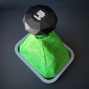 Op de afbeelding: Een groene suède versnellingspookhoes met een zwarte, diamantvormige versnellingspookknop met de letters "LII" erop.
