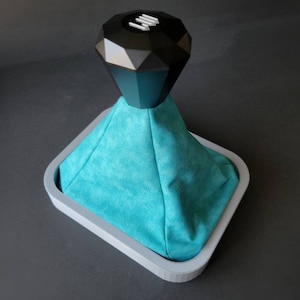 May include: A turquoise blue suede gear shift boot with a black diamond-shaped gear shift knob. The boot is sitting in a grey plastic base.
