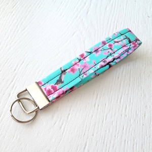 May include: A turquoise blue key chain with a floral pattern featuring pink cherry blossoms and a silver key ring.