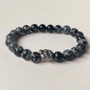 Op de afbeelding: Een armband van zwarte en witte gevlekte stenen kralen met een zilveren wolfshoofd bedel.