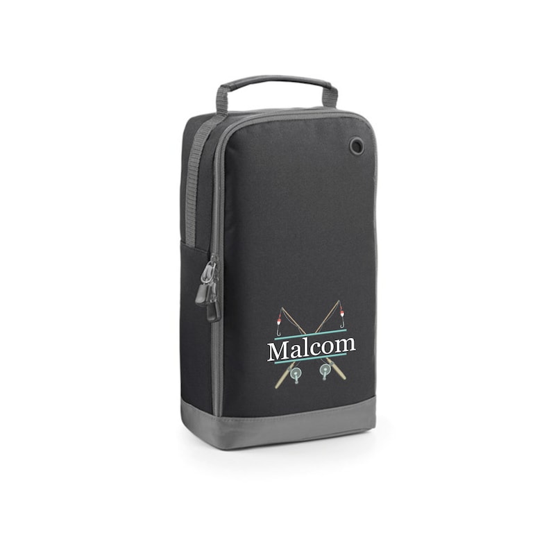 Puede incluir: Bolsa de zapatos negra con cierre de cremallera y asa gris. La bolsa tiene un dise&ntilde;o de ca&ntilde;a de pescar con el nombre "Malcolm" bordado.