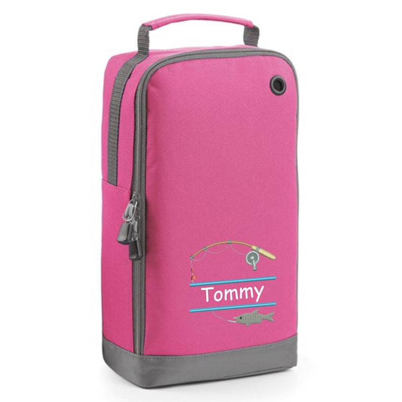 May include: Pink shoe bag with a zipper closure and a gray bottom. It features a fishing rod and fish design with the name "Tommy" embroidered on it.