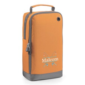 Puede incluir: Bolsa de zapatos naranja y gris con cierre de cremallera y asa. La bolsa tiene un dise&ntilde;o personalizado con dos ca&ntilde;as de pescar cruzadas y el nombre "Malcolm" escrito en blanco.
