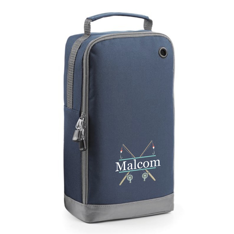 Puede incluir: Una bolsa para zapatos azul marino con un bolsillo lateral con cremallera y una base gris. La bolsa tiene un asa blanca y una inscripci&oacute;n blanca que dice "Malcolm" con un gr&aacute;fico de dos ca&ntilde;as de pescar cruzadas con flotadores rojos y anzuelos.