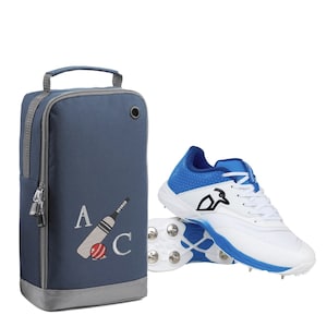 May include: A blue and gray shoe bag with a cricket bat and ball design and the letters "A" and "C". A pair of white and blue cricket shoes with spikes are in the background.