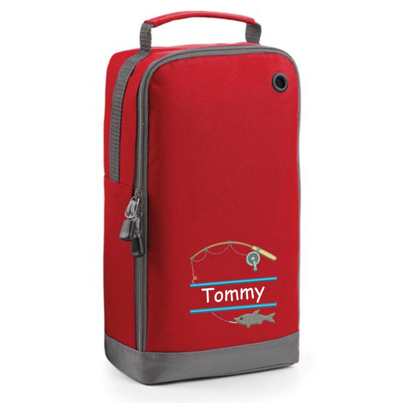 May include: Red shoe bag with a gray zipper and a gray bottom. The bag has a fishing rod and fish design with the name "Tommy" embroidered on it.