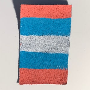 K&ouml;nnte beinhalten: Ein rechteckiges St&uuml;ck Stoff mit horizontalen Streifen in den Farben Rosa, Blau und Wei&szlig;.