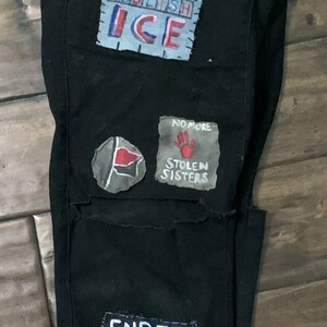 K&ouml;nnte beinhalten: Schwarze Jeans mit mehreren aufgen&auml;hten Patches. Die Patches haben verschiedene Botschaften, darunter "Abolish ICE", "No More Stolen Sisters" und "End the Hierarchy".