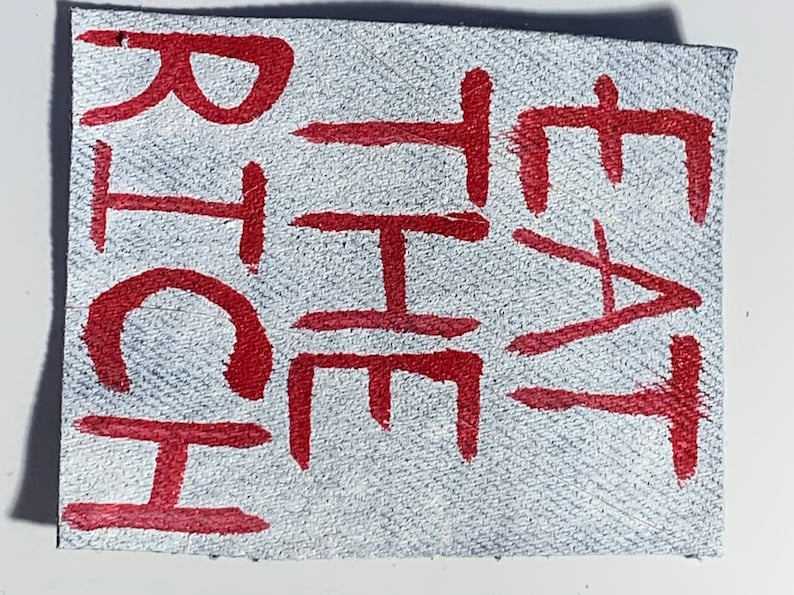 K&ouml;nnte beinhalten: Nahaufnahme eines wei&szlig;en Lederflicken mit dem Wort "CHEAT" in roter Farbe.