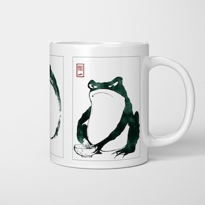 May include: White ceramic mug with a dark green frog illustration in a Japanese art style. The frog is depicted with a bowl. The mug has a white handle and a rectangular frame around the frog image. The word "Question" is in a red square.