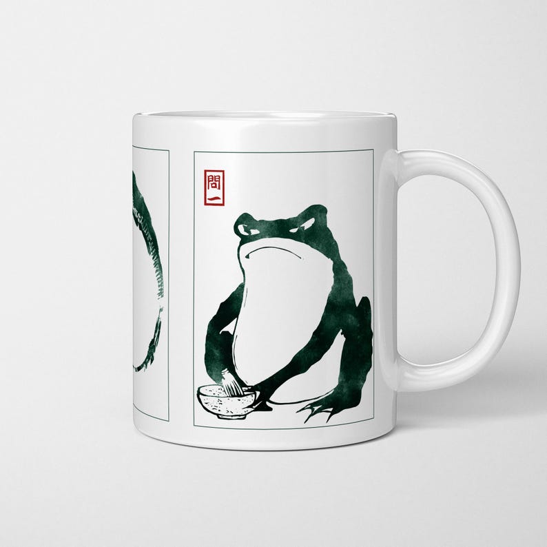 May include: White ceramic mug with a dark green frog illustration in a Japanese art style. The frog is depicted with a bowl. The mug has a white handle and a rectangular frame around the frog image. The word "Question" is in a red square.