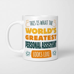 May include: White ceramic mug with a black and yellow design. The text on the mug reads "This is what the world's greatest personal assistant looks like".