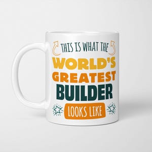 May include: White ceramic mug with a green, yellow and orange design. The text on the mug reads "This is what the world's greatest builder looks like".