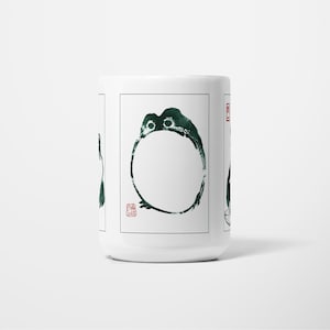 May include: White ceramic mug with a dark green ink illustration of a circular design with a stylized creature. The design includes a red stamp. The mug is a simple, elegant design.