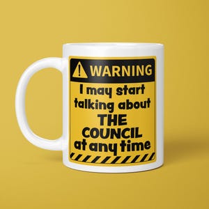 May include: A white ceramic mug featuring a yellow and black warning sign graphic. The text reads: WARNING I may start talking about THE COUNCIL at any time. The design includes a black triangle with an exclamation point and diagonal stripes.