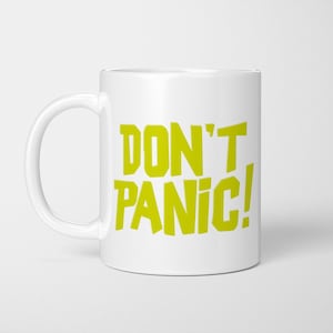 May include: A white ceramic mug featuring the text DON'T PANIC! printed in a bold, lime green sans-serif font. The mug has a standard cylindrical shape with a curved handle on the left side, providing a clear view of the graphic design.