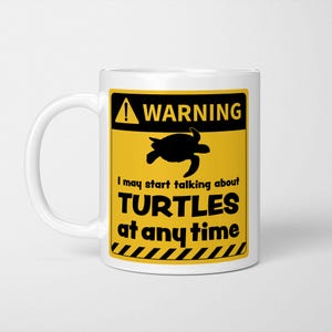 May include: A white ceramic mug featuring a yellow and black warning sign graphic. The design includes a black silhouette of a turtle and the text: WARNING I may start talking about TURTLES at any time, with black diagonal stripes at the base.