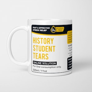 May include: White ceramic mug with a black and yellow label that reads "History Student Tears Saline Solution For Oral consumption only. 325ml/11oz". The label also includes a 0% alcohol free symbol.