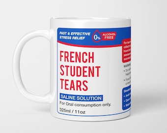 May include: A white ceramic mug featuring a blue and red label that reads "FRENCH STUDENT TEARS," "FAST & EFFECTIVE STRESS RELIEF," "0% ALCOHOL FREE," "SALINE SOLUTION," "For Oral consumption only," and "325ml / 11oz" with additional warning text.