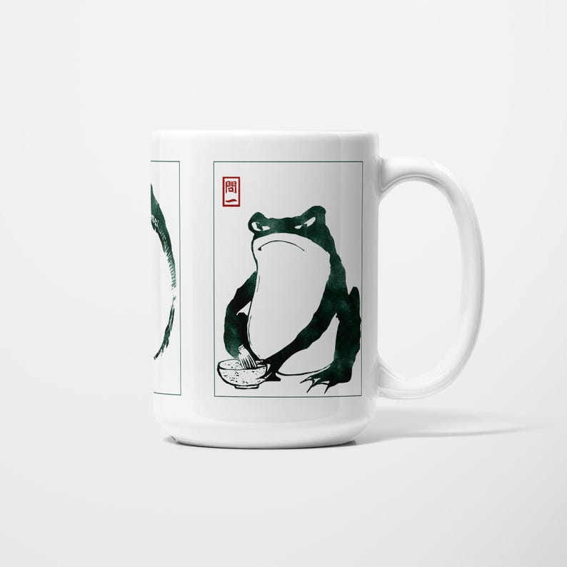 May include: White ceramic mug with a Japanese-style frog illustration. The frog is drawn in dark green ink, holding a bowl, and has a stern expression. A red Japanese character is also present on the mug.
