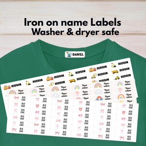 May include: A green t-shirt featuring iron-on name labels that are washer and dryer safe. The labels include designs of construction vehicles, rainbows, and pink bows with names like Daniel, Hudson, Piper Wilson, and Allie Lowe printed in black text.