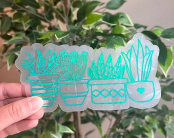 以下が含まれることがあります： 透明なステッカーに、緑色の輪郭で描かれた4つの鉢植えの植物が描かれています。植物はシンプルでスタイリッシュな方法で描かれており、どんな表面にも緑のアクセントを加えるのに最適です。