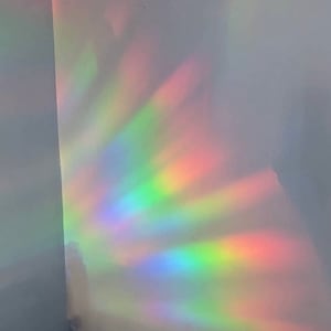 May include: A white wall with a rainbow prism light reflecting on it. The light is creating a colorful, iridescent pattern on the wall.