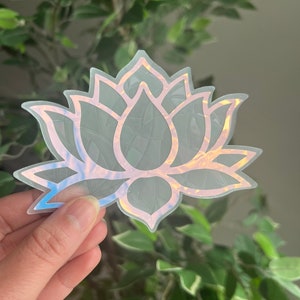 May include: A holographic sticker of a lotus flower with a white outline. The sticker has a iridescent finish that shifts colors in the light.