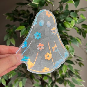 May include: A clear iridescent ghost sticker with a floral pattern in shades of blue and orange. The ghost has a simple, rounded shape and is perfect for adding a whimsical touch to any project.