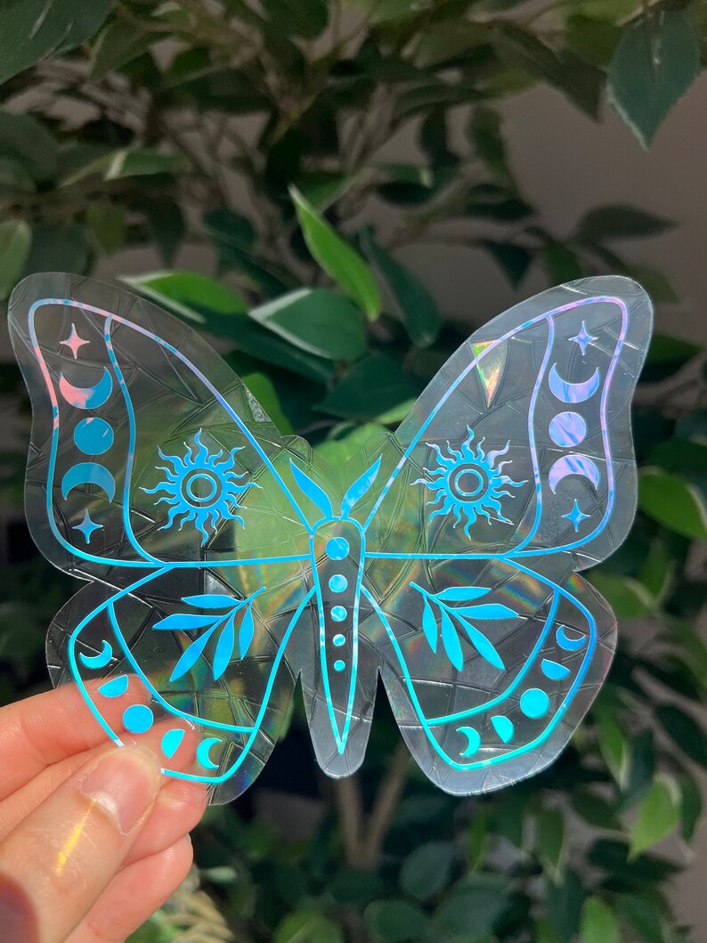 May include: A clear iridescent sticker of a butterfly with blue and white celestial designs, including moons, stars, and suns.