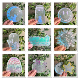 May include: A set of nine iridescent holographic stickers featuring various designs, including a crescent moon, a jar with a cat inside, a smiley face, a sun with mountains, a row of potted plants, a rainbow with the text "Let your light shine", a pumpkin, and a crescent moon with a star.