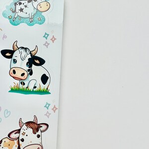 May include: A sheet of stickers featuring cartoon cows. The stickers have a white background with various cow designs, including a cow with a unicorn horn, a cow sitting in grass, and a cow with brown spots. The cows are in various poses and surrounded by stars.