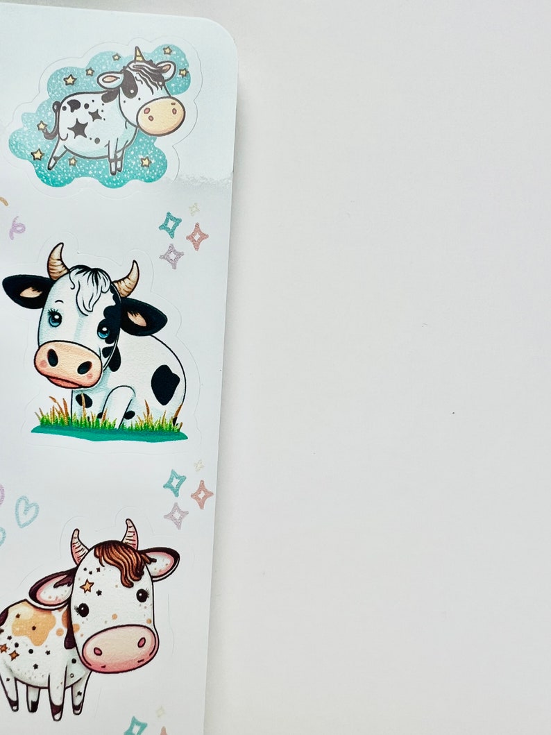 May include: A sheet of stickers featuring cartoon cows. The stickers have a white background with various cow designs, including a cow with a unicorn horn, a cow sitting in grass, and a cow with brown spots. The cows are in various poses and surrounded by stars.