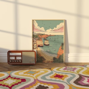 May include: A vintage-style illustration of a coastal scene with cliffs, a beach, and boats in the water. The illustration is framed in a light wood frame and hangs on a white wall.