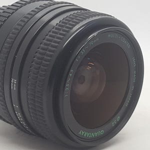May include: A black camera lens with a silver ring and the text "QUANTA RAY 0.53 MULTI-COATED 1:3.5-70mm 52mm MADE IN JAPAN" printed on it.