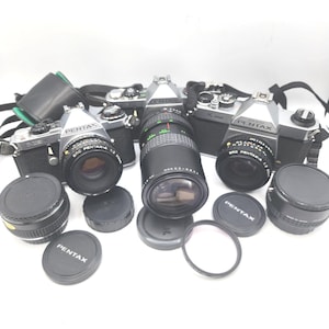 Könnte beinhalten: Eine Sammlung von Vintage Pentax SLR-Kameras und Objektiven. Die Kameras sind silber und schwarz, mit verschiedenen Objektiven und Objektivdeckeln. Eine schwarze Kameratasche ist im Hintergrund zu sehen. Die Objektive umfassen ein Zoomobjektiv und mehrere Festbrennweiten.