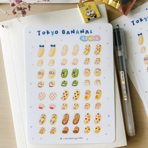 May include: A sheet of stickers featuring illustrations of Tokyo Banana, a popular Japanese pastry. The stickers feature various designs, including a banana with a blue bow, a banana with a heart, and a banana with a bear face. The text "Tokyo Bananas" and "東京ばな奈" are printed on the sheet.