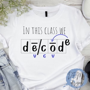 Puede incluir: Camiseta blanca con el texto "En esta clase decodificamos" con un diagrama que muestra la palabra "decodificar" desglosada en letras individuales y sus sonidos de vocales y consonantes.
