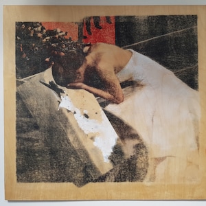 May include: A black and white photograph of a person in a white dress, with their head resting on a surface. The image is printed on a wooden panel.