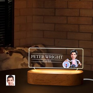 May include: A wooden base with a clear acrylic panel displaying a cartoon image of a person with the text "Peter Wright Engineer".